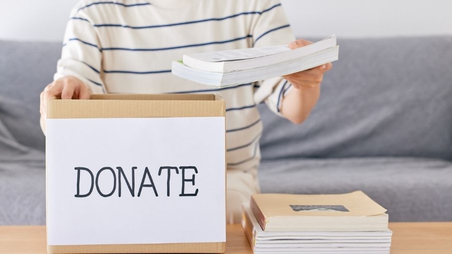 A person putting books in a box labeled “donate.” A person putting books in a box labeled "donate."